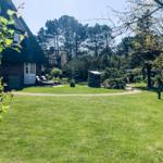 Green lawn with sun loungers in front of a house with thatched roof.