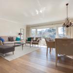 Living and dining area with wooden floor, sofa, chairs, and windows.