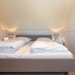 Zimmer mit Doppelbett, Nachttischen und Lampen unter schrägen Wänden.