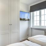Bedroom with white bed, window, and wall-mounted TV.