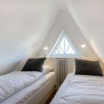 Two beds under a skylight with two nightstands and lamps.