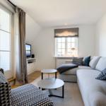 Living room with sofa, tables, and windows. Outdoor area visible.