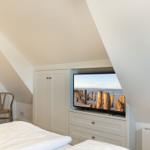 Bedroom with sloped ceiling, bed, chair, and TV showing beach.