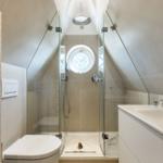 Shower with glass enclosure, round window, and sink with mirror.