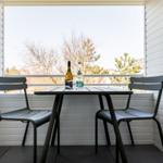 Balcony with table and two chairs, bottle and glass on table, view of trees.