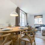 Dining area with round table and chairs. Living area with sofa and windows.