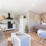 Living area with kitchen and bedroom. Wooden floor, white refrigerator, and bed with headboard.