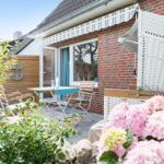 Terrace with table, chairs, and white awning in front of red brick house.
