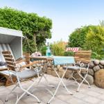 Terrace with lounge chair, table and chairs. Background: stone wall and green plants.