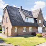 House with brick facade, dark roof, and white entrance. Lawn and paved path.
