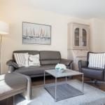 Living room with sofa, armchair, and coffee table. Kitchen in background.