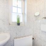 Bathroom with marble walls, sink, mirror, and plant by the window.