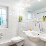 Bathroom with sink, toilet, and window. Green bottles are on the shelf.