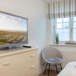 Bedroom with TV, chair, and window with blinds.