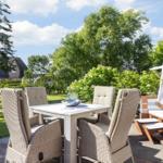 Terrace with dining table, chairs, and beach chair. Lawn and trees in background.