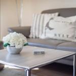 Living room with gray sofa, table, and flowers. Pillow with Sylt logo.