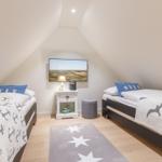 Two single beds with Sylt bedding, TV, and small nightstand.
