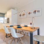 Dining area with wooden table, white chairs, and wall art
