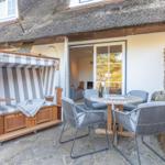 Terrace with beach chair, table and chairs in front of a house with thatched roof.