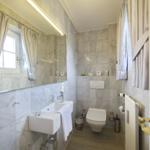 Bathroom with sink, toilet, and mirror. Tiled wall and window with curtains.
