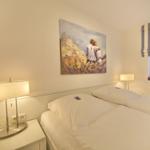 Two beds with white sheets, wall painting, and window with striped roller blind.