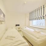 Two beds with white linens and towels. Window with striped roller blind and white rabbit figurines.