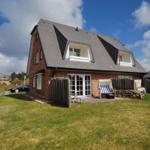 A house with red brick, gray roof, and terrace with lounge chair.