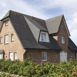 Two-story brick house with dark roof and white windows. Front garden with rose hedge.
