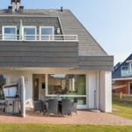 Haus mit Terrasse, Grill und Sitzgelegenheiten im Freien.