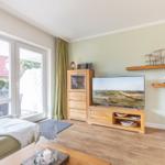 Wohnzimmer mit Fernseher, Holzmöbeln und Blick auf Terrasse.