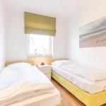 Zwei Einzelbetten mit weißen Bettwäsche, Fenster mit grünem Rollladen und Wandbild.
