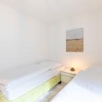Zwei Betten mit weißen Laken, Nachttisch mit Lampe und Wandbild.