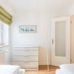 Schlafzimmer mit weißem Schrank, Fenster mit grünem Rolladen und offener Tür.