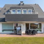 Haus mit Balkon, Terrasse und Gartenbereich mit Sitzgelegenheiten.