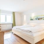 Ein Schlafzimmer mit Doppelbett, Fenster, grünen Vorhängen und Wandbild.