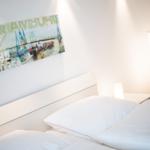 Schlafzimmer mit weißem Bett, Wandbild und Stehlampe.