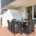 Terrasse mit Gartentisch und sechs Stühlen, umgeben von weißem Zaun und rotem Pflaster.