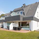 Moderne Villa mit Balkon, Terrasse und Garten. Große Fenster und schwarz-weiße Fassade.