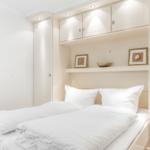Bedroom with white bed and built-in cabinet above the headboard.