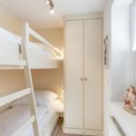 Room with bunk bed, wardrobe, and window with blinds.