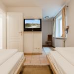 Zwei Betten, Fernseher und Fenster mit Vorhängen.