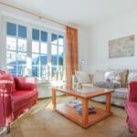 Wohnzimmer mit roten Sesseln, Sofa und Glas-Tisch. Fenster mit Vorhängen.