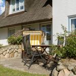 Terrasse mit Tisch, Stühlen und Strandkörben vor einem Haus mit Strohdach.