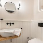 Badezimmer mit Waschbecken auf Holz, Spiegel und Wandbeleuchtung.