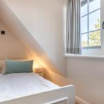 Schlafzimmer mit Dachschräge, Bett und Fenster mit Blick auf Bäume.