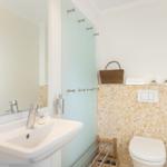 Badezimmer mit Waschbecken, Spiegel, Toilette und Mosaikwand