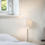 Schlafzimmer mit Bett, Stehlampe und Fenster mit Blick auf Grün.