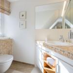 Badezimmer mit Waschbecken, Spiegel und Toilette. Fenster mit Blick nach draußen.