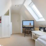 Schlafzimmer mit Dachschräge, TV und Fenster. Weiße Einbaumöbel und Bett.