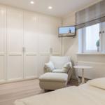Schlafzimmer mit Bett, Sessel, Kleiderschrank und TV. Fenster mit Rollladen und Pflanzen.